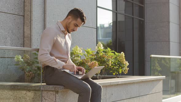 Hispanic Businessman Sitting Outside with Laptop Working Remote Distant Job Outdoors Near Office alt