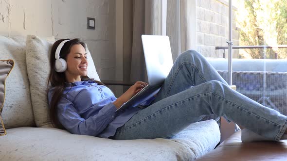 Pretty girl using laptop on couch at home in the living room. Listening music, relaxation after a ha alt