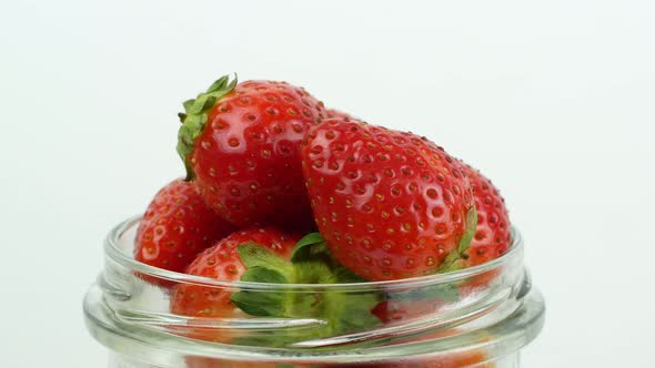 4K glass jar with red ripe strawberries rotating on a white background. Ripe summer red strawberry