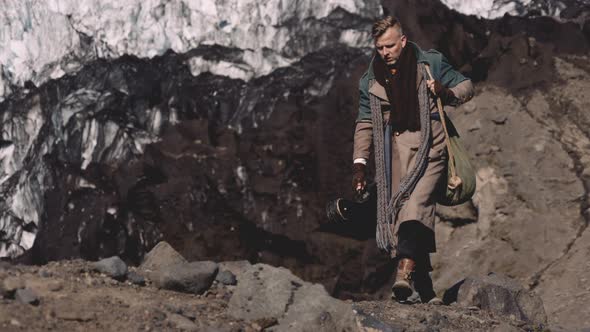 Man With Guitar Walking Along Rocks By Glacier alt