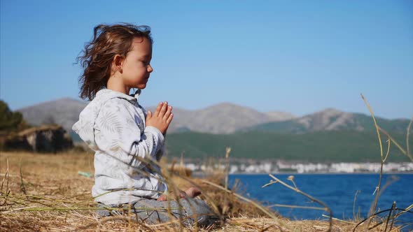 Cute Little Child Gurl Meditating Alone in Lotus Pose at Lake Shore alt