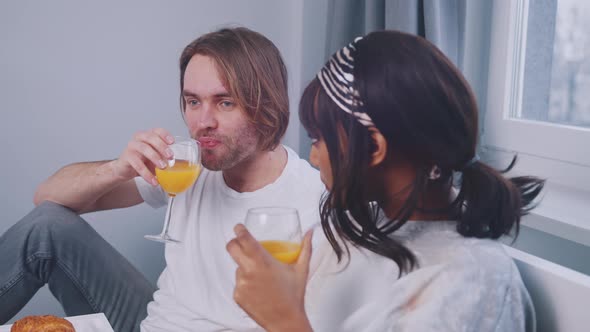 Young Multiracial Couple Drinking Orange Juice and Having Conversation in the Bed alt
