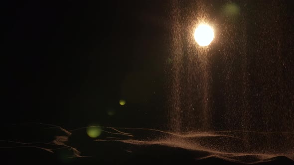 Particles of Dry Sand are Pouring Down on Black Studio Background with Backlight alt