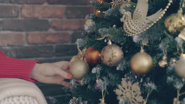 Young Woman Touches Golden Ball and Bow on Christmas Tree alt