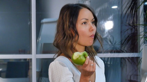 Pretty businesswoman eating green apple in the office