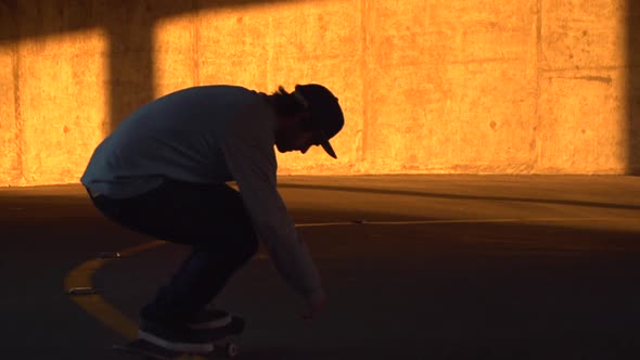 Silhouette of a young man skateboarding in a parking garage at sunset. alt