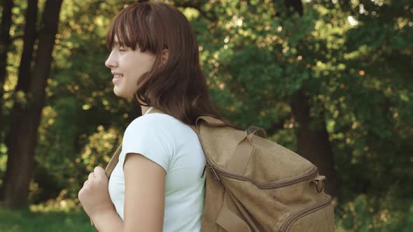 Girl Traveler Is Walking Through the Woods with a Backpack. Happy Hiker Girl in Summer Park alt