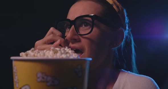 Woman with glasses watching a scary horror movie at the cinema and eating popcorn