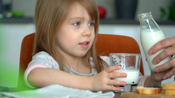 Girl Pours Milk From Bottle Into Glass and Drinks Milk on Kitchen
