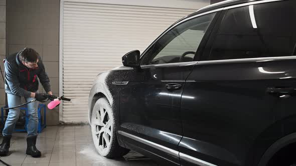 Male Car Expert Covering Dark Luxury Auto with Foam at Washing Service alt