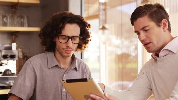 Two men using digital tablet in cafe alt