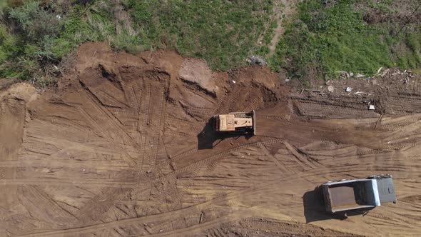 Top aerial view of bulldozer flattening surface on further construction site alt