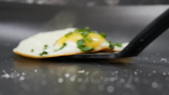 the Cook Removes the Fried Egg with Onions From the Pan Using a Black Culinary Spatula