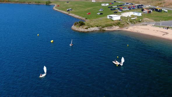 people practicing in the sailing school of the lake with beach, parking full of cars. Tiro de drone alt