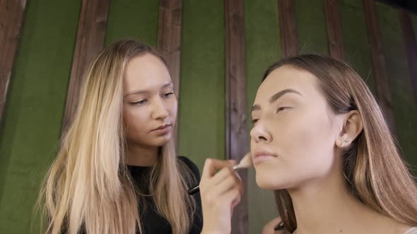 Attractive Caucasian Makeup Artist Doing Makeup for Asian Female in Beauty Salon