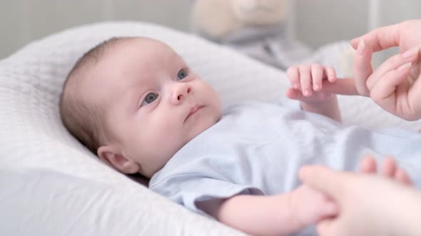 Newborn Baby Boy Lying in Nursery Cocoon with Blue Clothes on Bed in Bedroom at Home Looking to alt