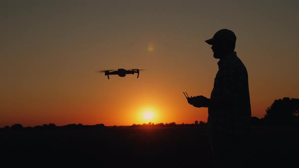 Silhouette of a Man at Sunset Takes Off a Drone alt