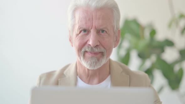 Close Up of Old Man Smiling at Camera While Using Laptop in Office alt