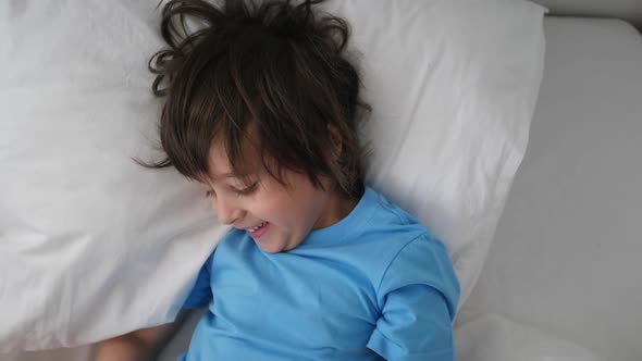 Boy Child in a Blue Tshirt Lies on a White Bed