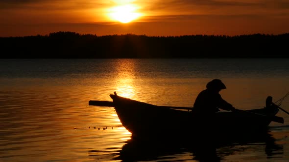 Silhouette of Fisherman Rowing on Boat at Sunset