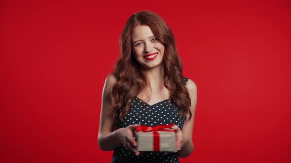 Joyful Beautiful Woman with Perfect Makeup Holding Gift Box with Bow on Red alt