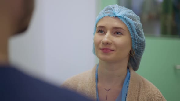 Portrait of Confident Young Caucasian Beautiful Woman in Surgical Cap Talking with Unrecognizable alt
