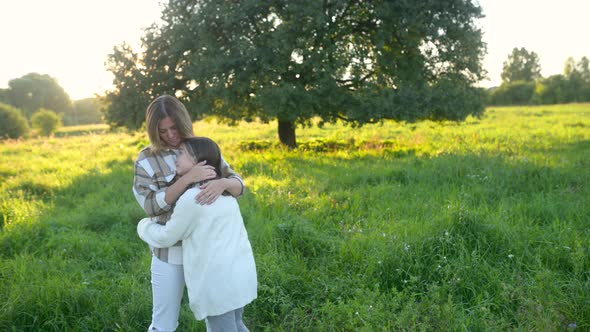 Loving tender mum hugging with a cute daughter on a field at sunset