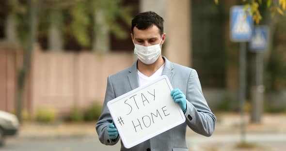 Young men wearing a face mask and gloves holding board with stay at home text.