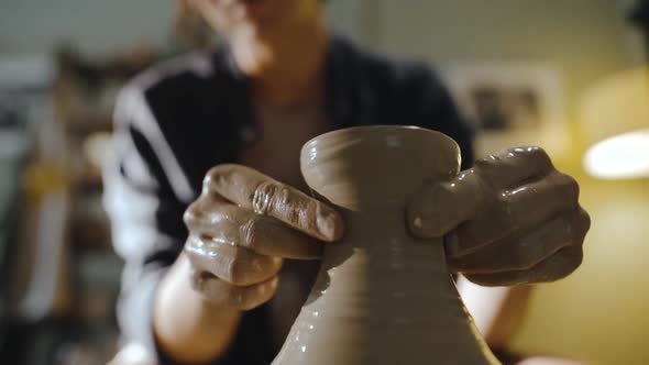 Young Female Potter Gently Pulls the Neck of a Clay Vessel on a Potter's Wheel
