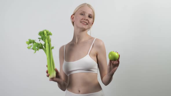 Young Slender Woman Dances Vigorously with a Green Apple and Celery in Her Hands
