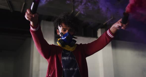 Mixed race man holding blue and purple flares standing in an empty building alt