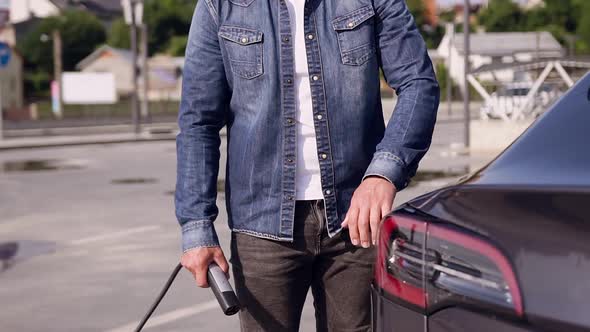 Modern Guy Charging His Trendy Electric Car at Specially-Equipped Charging Station alt