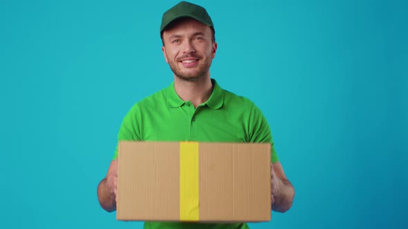 A Young Male Courier in a Green Uniform Holds a Parcel in His Hands