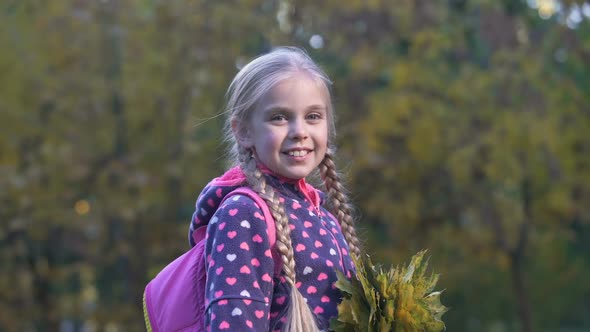 Beautiful Schoolgirl With Autumn Leaves Looking at Camera and Showing Thumbs Up alt
