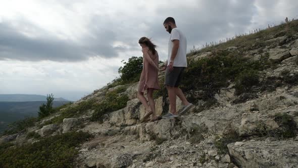 A Young Couple Holding Hands Walks Along the Mountainous Terrain To the Slope