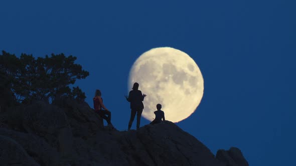Silhouette of Three People on Rocks Opposite Huge Moon