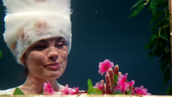 Closeup Portrait of Pretty Woman Underwater Fairytale Flower Fairy is Sniffing Blossom in Subaquatic alt