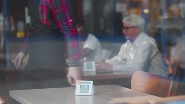 View Though Window of Waiter Put Qrcode Sign for Online Menu on Table in Restaurant alt