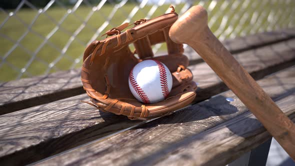 Baseball mitt with ball and bat at a wooden bench. Sports gear. American sport. alt