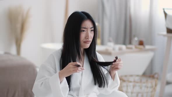 Young Upset Asian Woman Looking at Her Split Ends and Frowning Face Feeling Displeased of Her alt