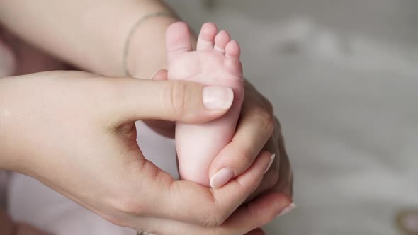 Close up of beautiful young female hands hold and caress little cute foot of newborn baby. 