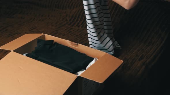 Young Girl Collects a Parcel With Things and Examines Clothes alt