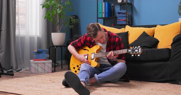 Young Student Boy Plaing on Guitar Sits on the Floor at Home alt