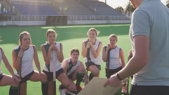 Hockey coach explaining game plan with female players on the field alt