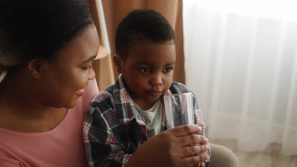 Caring Black Mother Giving Her Preschooler Son Glass Of Water At Home alt