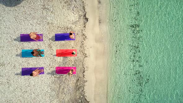 Aerial view of group of people doing yoga on colorful mats on sandy beach. alt