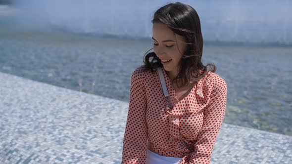 Portrait of Beautiful Girl in Colorful Summer Clothes Sitting Near a Fountain alt