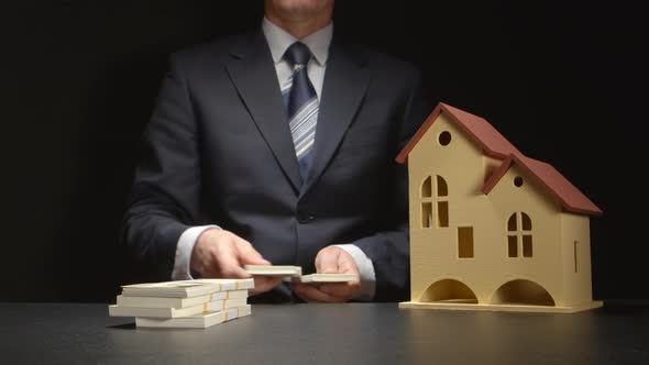 Businessman counts a money and near a house model on a table