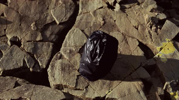 Black Trash Bag Lay on a Rocky Beach alt