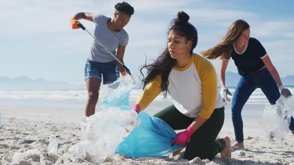 Diverse group of female friends putting rubbish in refuse sacks at the beach alt